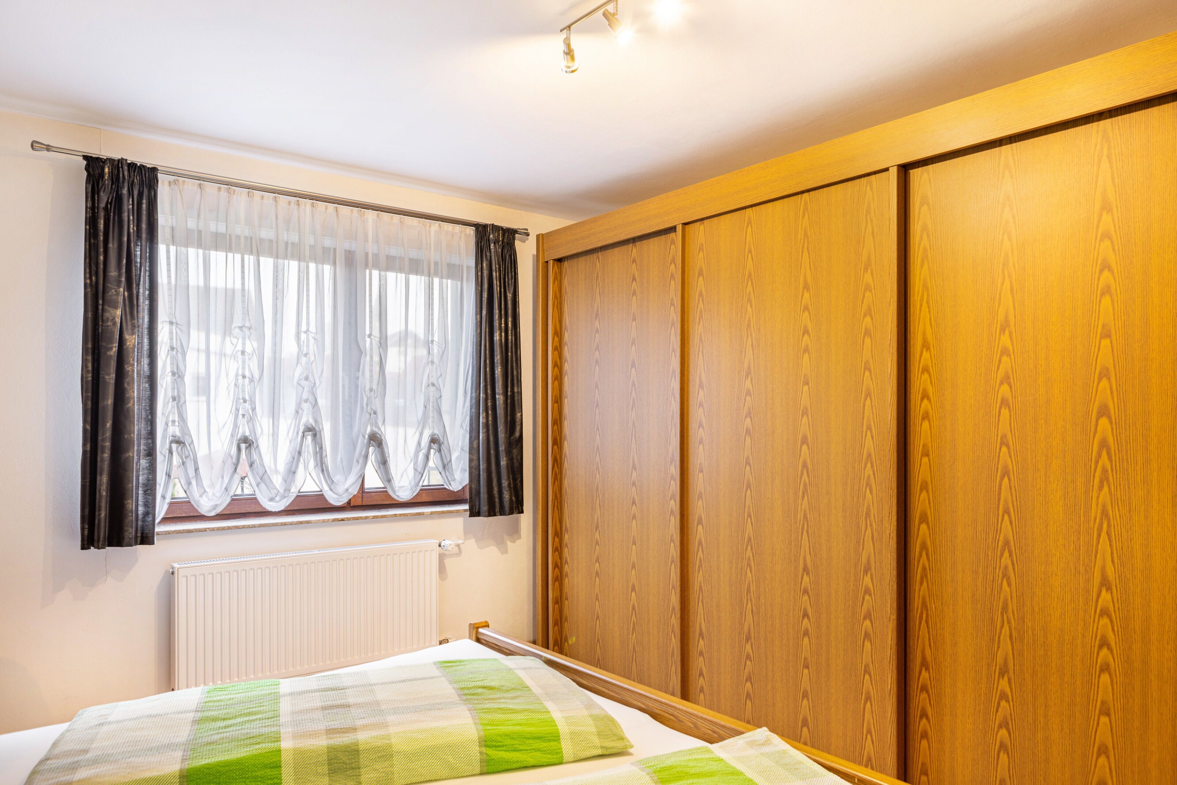 Un dormitorio con cama, ventana con cortinas, radiador y puertas de armario de madera.