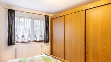 Un dormitorio con cama, ventana con cortinas, radiador y puertas de armario de madera.