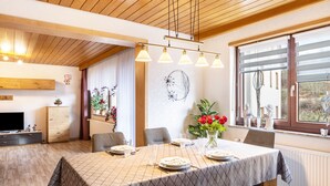 A dining area with a table set for four, wooden ceiling, and a large window with blinds.