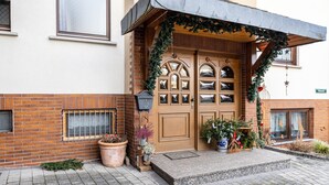 A building with a wooden front door, a brick facade, and a small porch area with potted plants.