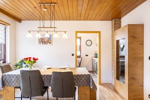 A dining area with a wooden ceiling, a table with a patterned tablecloth, chairs, a vase of flowers, and a clock on the wall. - Holiday Apartment 'Göpfert' with Wi-Fi (Ebersburg-Weyhers)