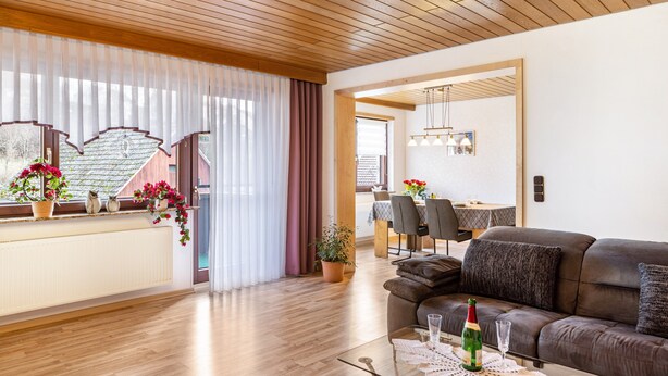 A modern living room with a sofa, a dining area, and a kitchen visible through an open door.