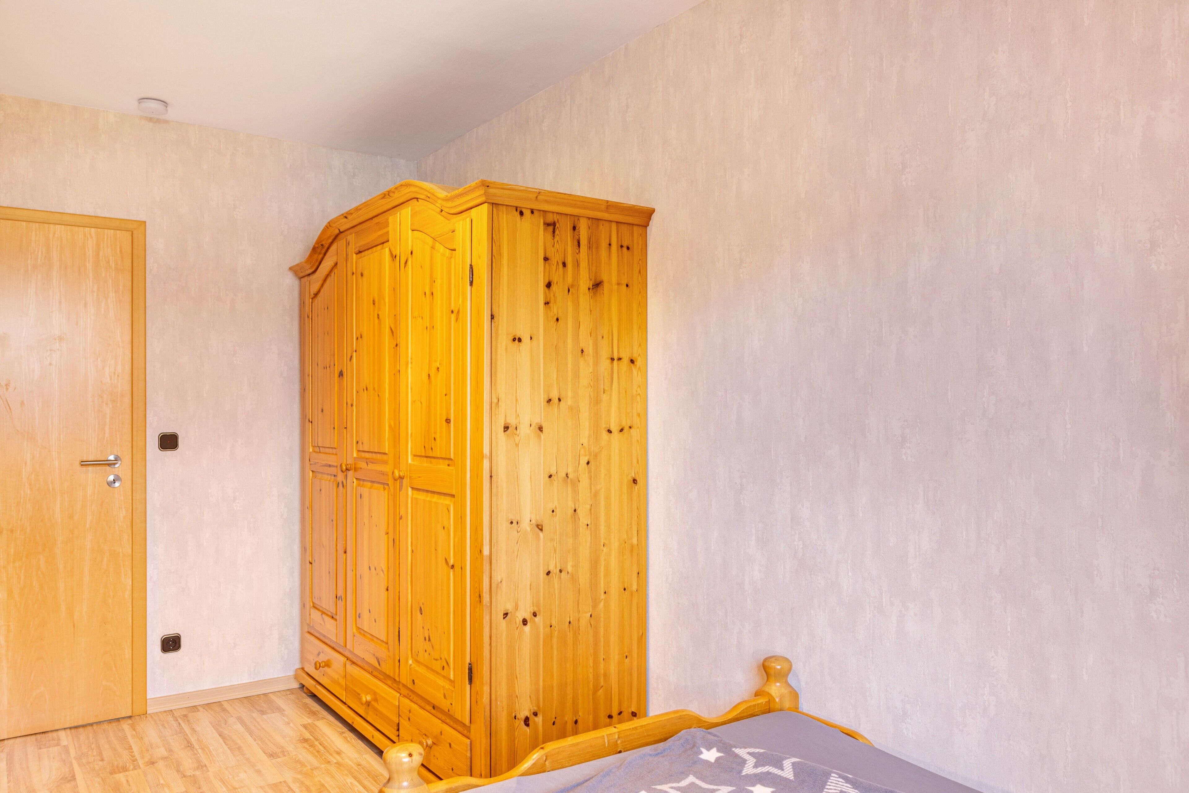 Un dormitorio con un armario de madera, una cama con cabecera y una puerta.