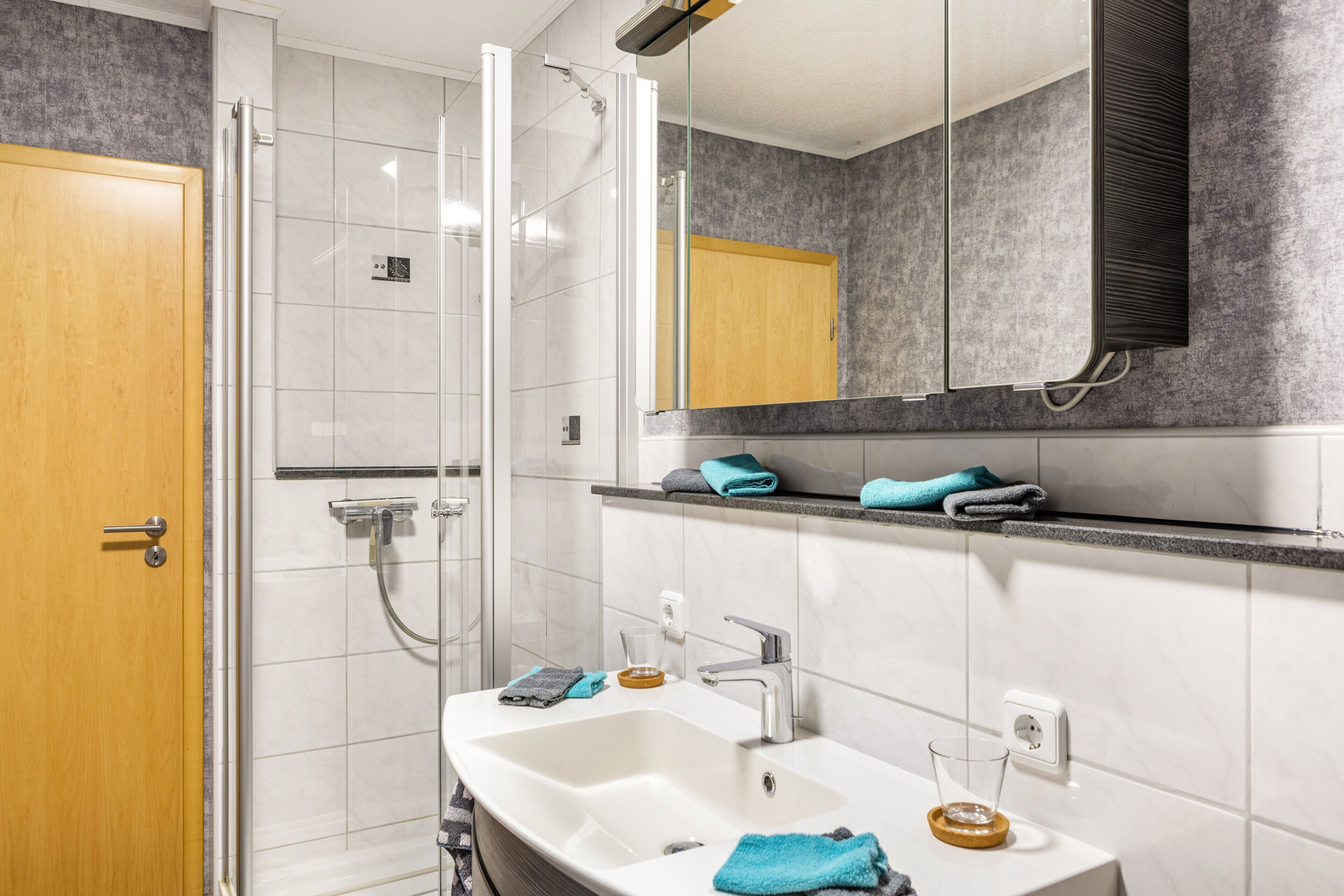 Een badkamer met een douche, twee wasbakken, een spiegel en een handdoekhouder.