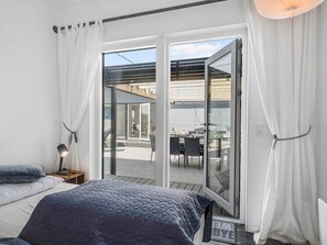 A bedroom with a bed, a nightstand, a lamp, and a sliding glass door leading to an outdoor patio area. - 5 Star Holiday Home in Vaeggerlose (Vaeggerlose)