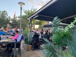 An outdoor dining area with tables and chairs, surrounded by potted plants and a covered walkway. - 5 Star Holiday Home in Vaeggerlose (Vaeggerlose)