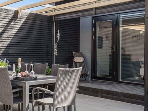 An outdoor patio with a table set for dining, wicker chairs, and a glass door leading to an interior space. - 5 Star Holiday Home in Vaeggerlose (Vaeggerlose)