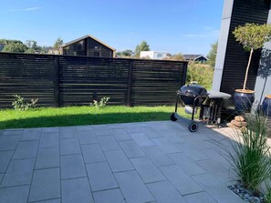 A backyard with a paved patio, a barbecue grill, and a wooden fence. - 5 Star Holiday Home in Vaeggerlose (Vaeggerlose)