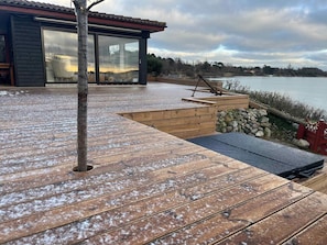Een houten terras met een stenen muur en een glazen deur die naar een kamer leidt.