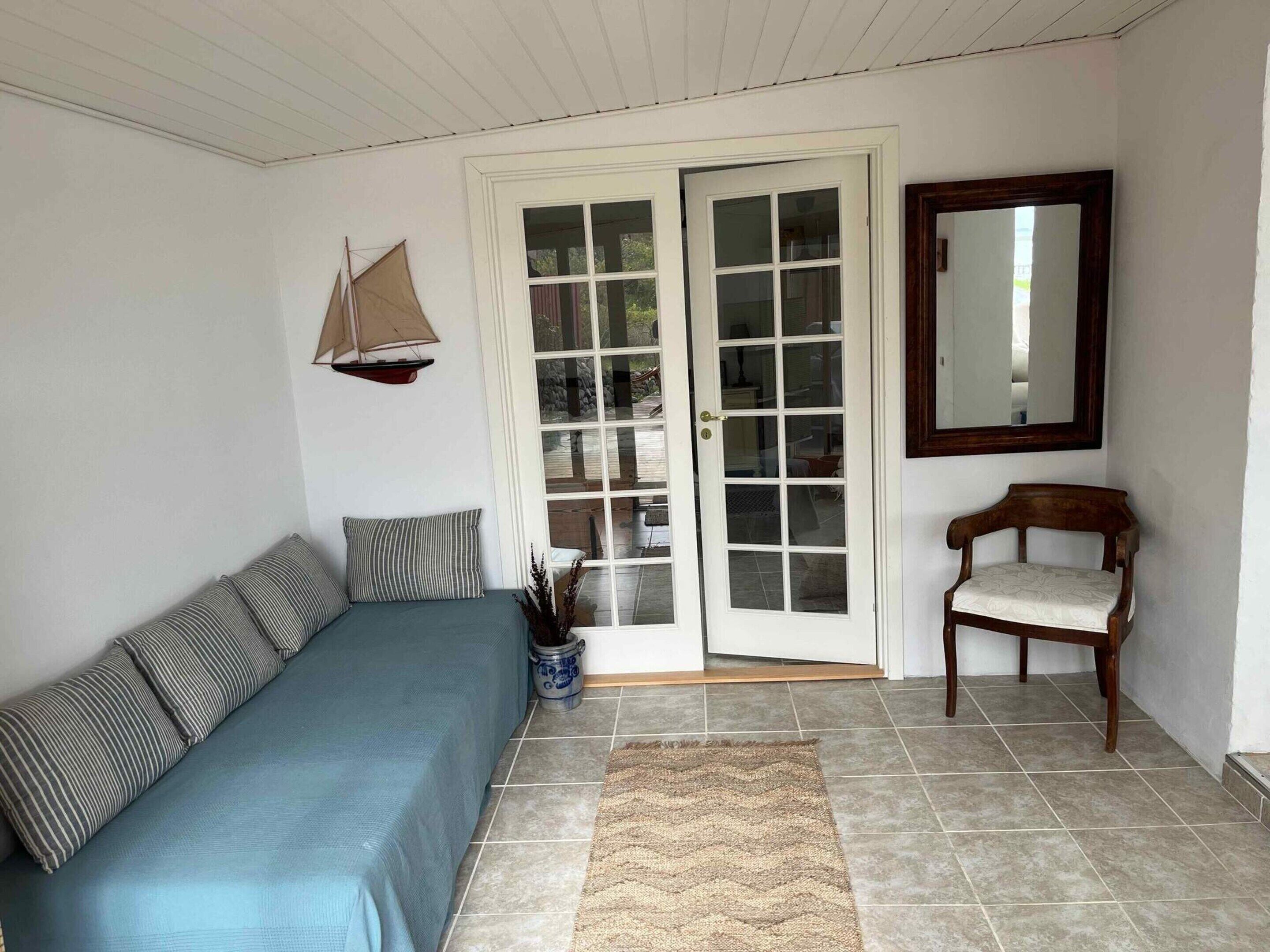 A room with a sofa, a chair, a large window with a sailboat decoration, and a tiled floor.