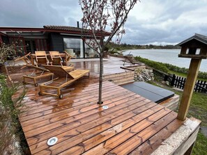 A wooden deck with lounge chairs and a small tree, overlooking a body of water. - 5 Star Holiday Home in Martofte (Martofte)