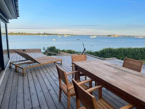A wooden deck with a table and chairs overlooking a calm body of water with boats. - 5 Star Holiday Home in Martofte (Martofte)