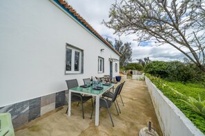 A patio with a table set for dining, a white building with a tiled roof, and a garden with various plants. - Villa 'Sunrise' with Private Terrace, Private Garden and Wi-Fi (Carvoeiro)