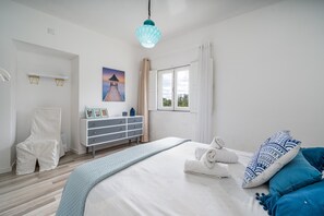 A bedroom with a bed, a chair, a dresser, a window, and a painting. - Villa 'Sunrise' with Private Terrace, Private Garden and Wi-Fi (Carvoeiro)