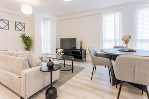 En moderne stue med sofa, sofabord, fjernsyn og et spiseområde med stole og bord.