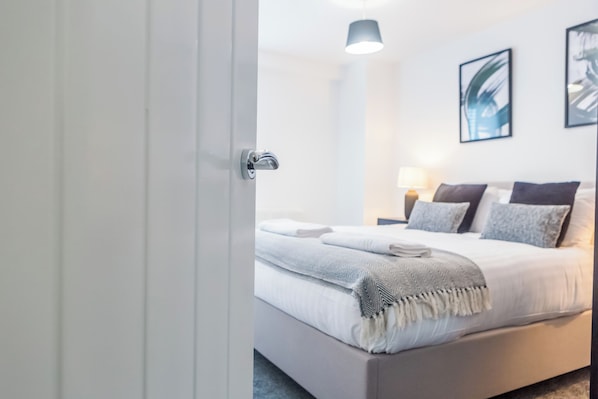 Um quarto moderno com uma cama bem arrumada, abajur e quadros nas paredes.