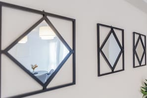 En væg med tre geometriske spejle i rammer og et spiseområde med et bord og stole.