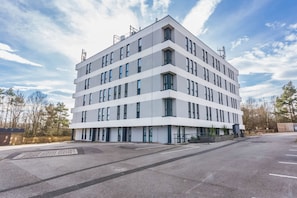 Um edifício moderno de vários andares com telhado plano, grandes janelas e estacionamento em frente.