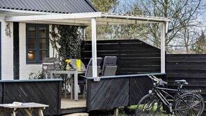 A covered outdoor seating area with a table and chairs, a bicycle, and a wooden deck. - 5 Star Holiday Home in Nexo (Nexø)