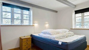 A bedroom with a bed, wooden nightstand, and two windows with curtains. - 5 Star Holiday Home in Nexo (Nexø)
