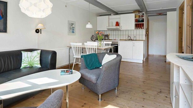 A modern living room with a sofa, a dining table, and a kitchen in the background. - 5 Star Holiday Home in Nexo (Nexø)