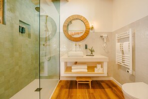 A modern bathroom with a glass-enclosed shower, a round mirror, a white sink, and a toilet. - Chalet do Lago (Ponte de Sor)