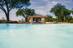 A poolside cabana with a thatched roof, a dining area, and lounge chairs. - Chalet do Lago (Ponte de Sor)