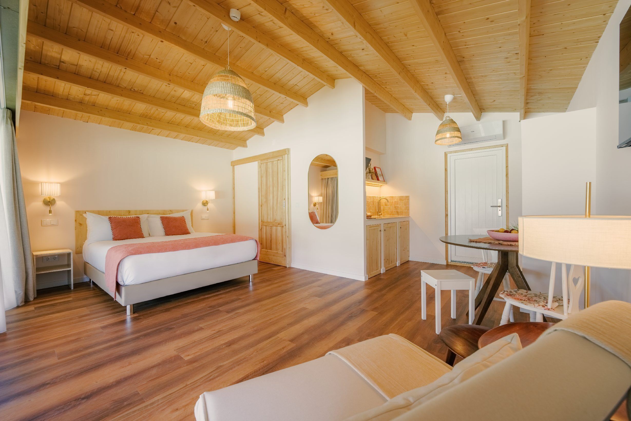 A spacious bedroom with a large bed, a sitting area with a table and chairs, and a kitchenette in the background.
