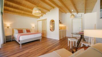 A spacious bedroom with a large bed, a sitting area with a table and chairs, and a kitchenette in the background.