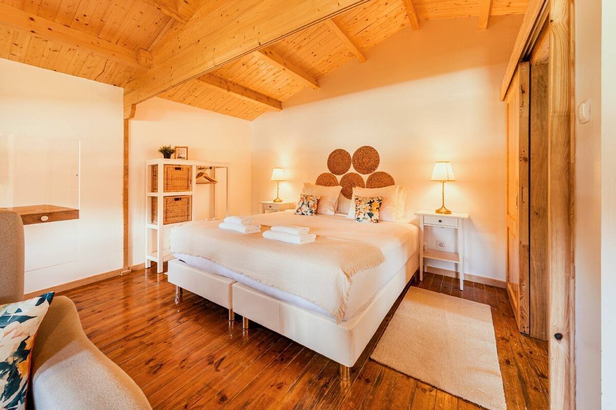 A bedroom with a wooden ceiling, a large bed with white bedding, two bedside tables with lamps, and a wooden floor.