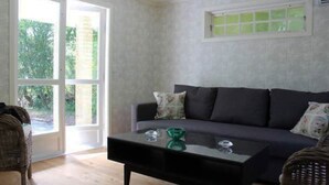 Un salon avec un canapé foncé, une table basse en verre et un fauteuil en osier.