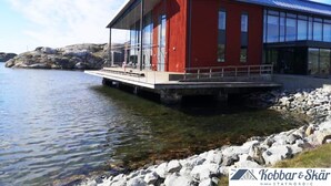 Un bâtiment rouge à la façade en verre, situé sur une côte rocheuse, au bord de l’eau.