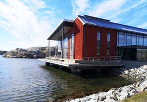 Un bâtiment rouge à la façade en verre, situé sur une côte rocheuse, au bord de l’eau.