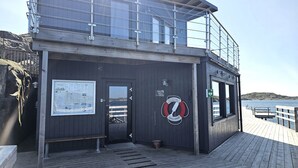 A wooden building with a lifebuoy, a sign, and a bench. - Two charming cottages in Hälleviksstrand | SE09133 (Hälleviksstrand)