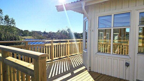 A wooden deck with a railing, a window, and a clear view of a blue-roofed building in the background. - Family-friendly house close to sea & nature in Klövedal | SE09145 (Klövedal)