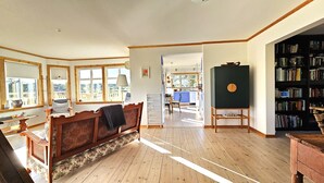 A spacious living room with a wooden floor, a sofa, a bookshelf, and a dining area. - Family-friendly house close to sea & nature in Klövedal | SE09145 (Klövedal)
