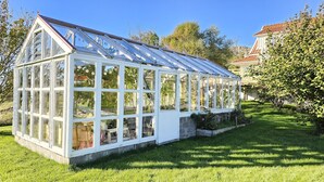 A large, white greenhouse with multiple windows and a sloped roof, surrounded by a well-maintained lawn. - Family-friendly house close to sea & nature in Klövedal | SE09145 (Klövedal)