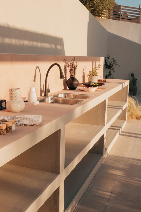 A modern kitchen with a long countertop, stainless steel sink, and various kitchen items.