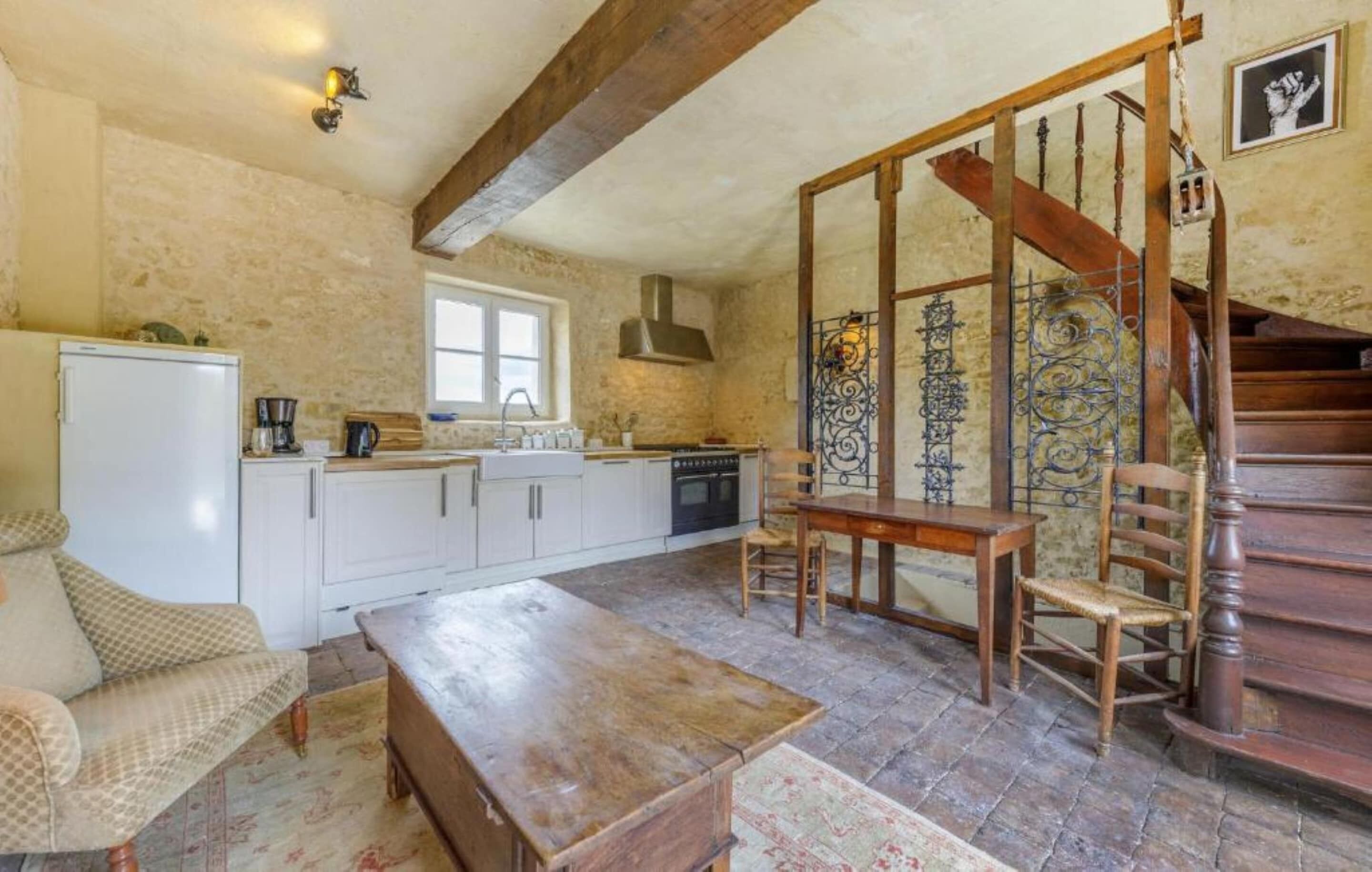 Een rustieke keuken met een houten tafel, een bank en een trap.