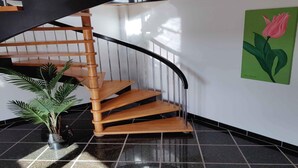 A spiral staircase with wooden steps and black railings, a potted plant, and a painting of a pink tulip on the wall. - 5 Star Holiday Home in Galten (Galten)