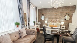 Un salon moderne avec un canapé, une table à manger et des chaises. On y trouve deux miroirs, un lustre et une plante.