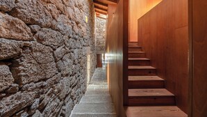 Um corredor de paredes de pedra com degraus de madeira que levam a uma porta de madeira.