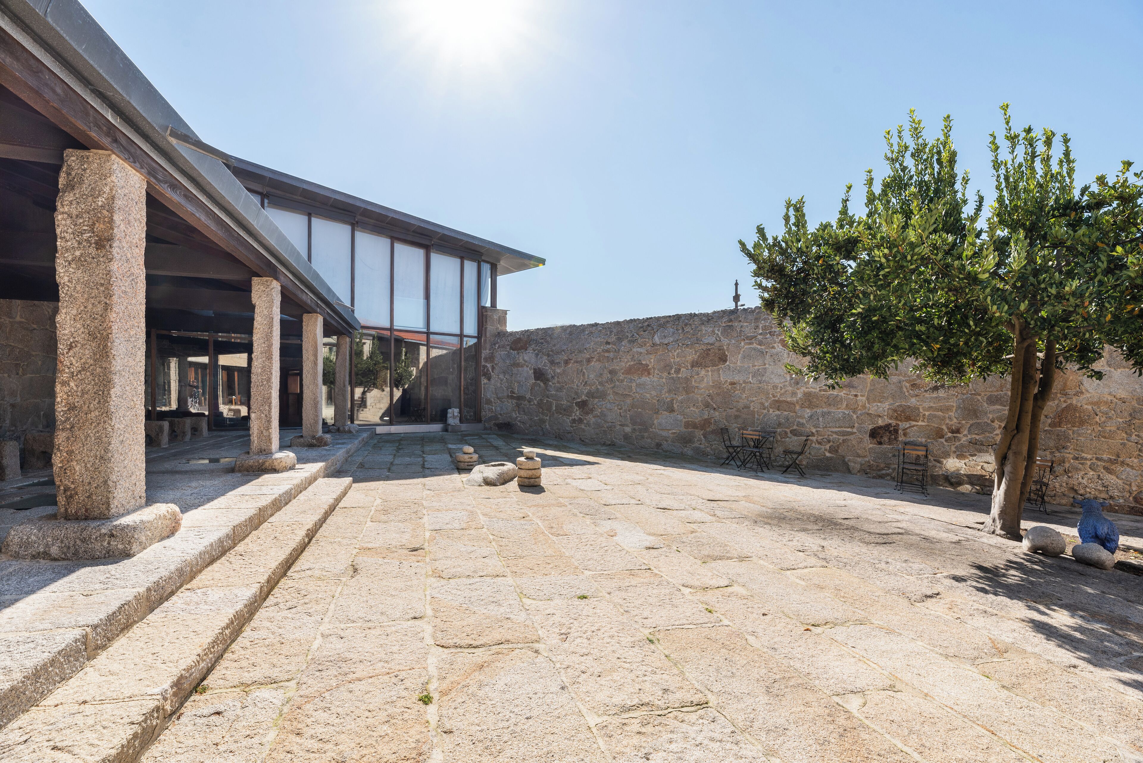A courtyard with stone columns, a stone wall, and a tree.