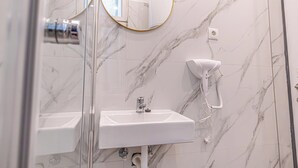 Une salle de bain avec un lavabo blanc, un sèche-cheveux fixé au mur et un miroir avec un cadre doré.