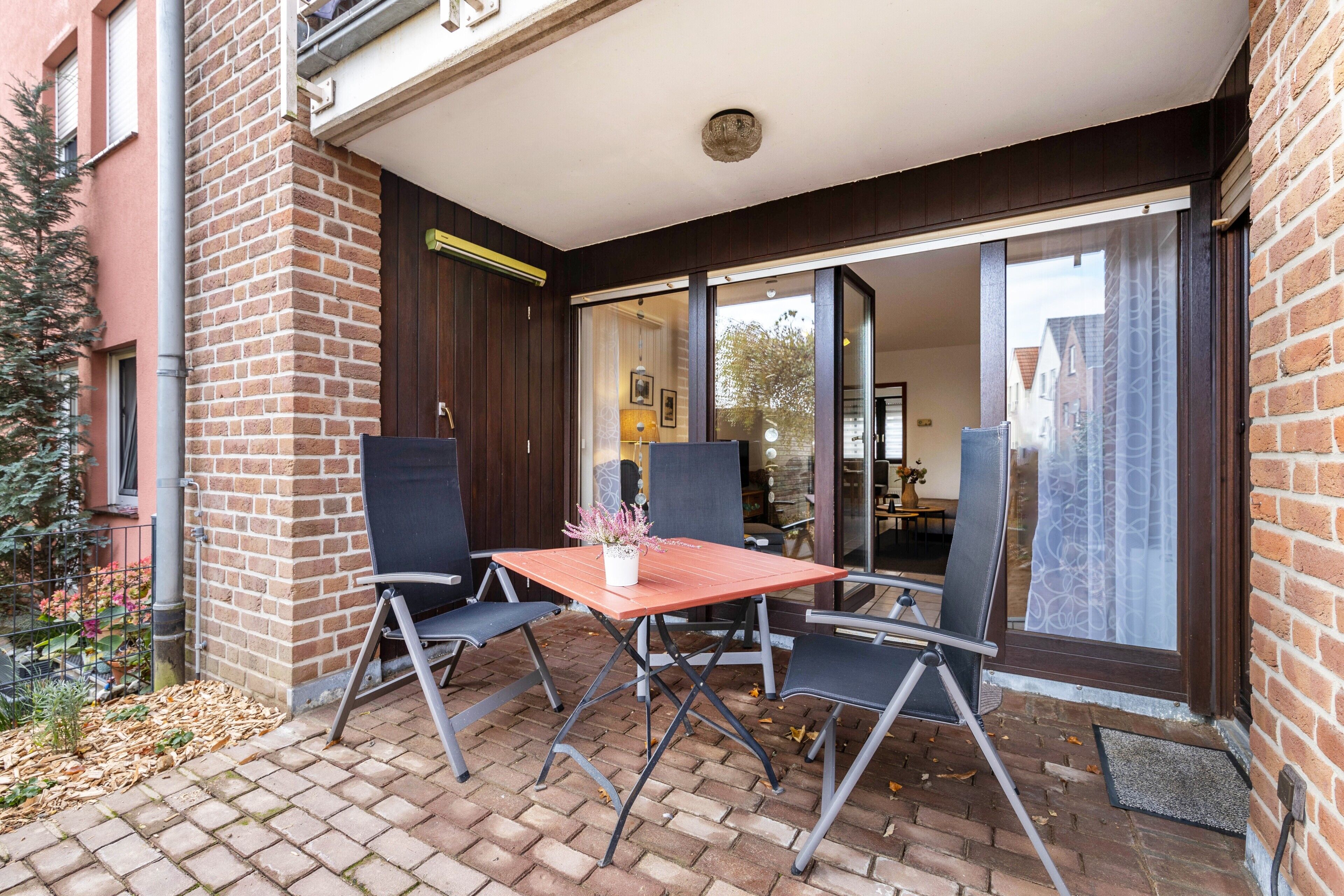 Eine Terrasse mit Tisch und Stühlen, eine Ziegelmauer und eine Schiebetür zu einem Innenbereich.