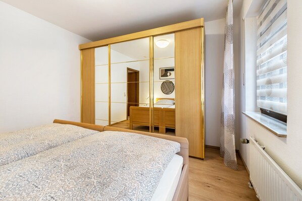 Una camera da letto con un letto, un armadio in legno, una scrivania e una finestra con persiane.