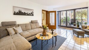 Ein modernes Wohnzimmer mit einer Eckcouch, zwei Couchtischen, einem Stadtbild und einer großen Schiebeglastür, die zu einem Außenbereich führt.