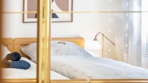 Ein ordentlich bezogenes Bett mit einer gemusterten Decke, einer Nachttischlampe und einem gerahmten abstrakten Kunstwerk an der Wand.