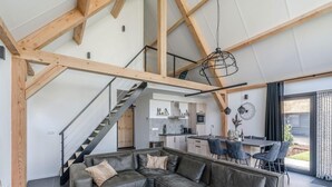 Un intérieur moderne avec des poutres apparentes, un canapé d’angle, un coin repas et une cuisine.