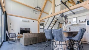 Un espace de vie moderne doté d’un plafond haut, d’un escalier, d’un coin cuisine et d’un espace salon avec des tabourets de bar.